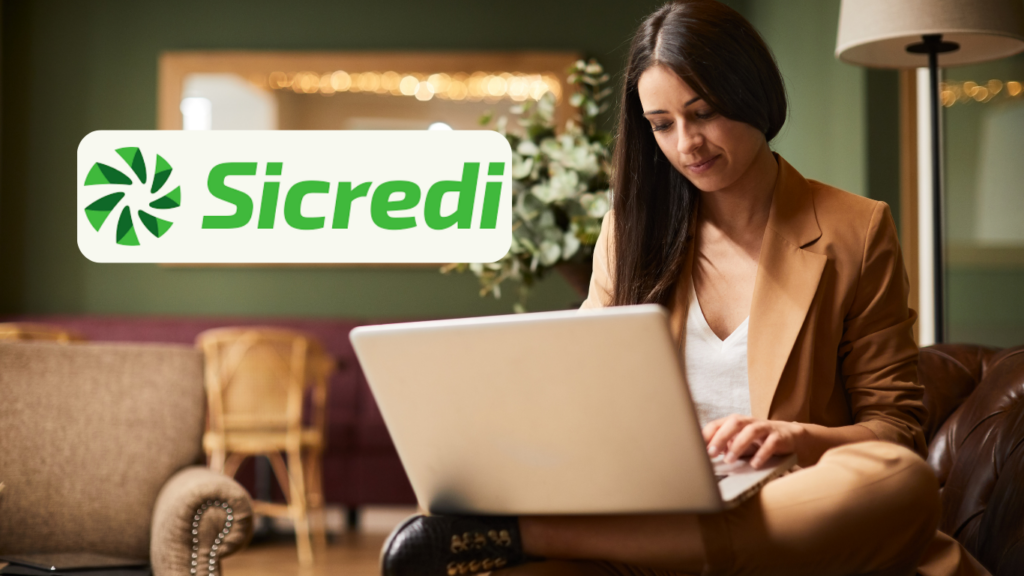 Uma mulher com um traje bege está sentada em um sofá, concentrada enquanto usa seu laptop. A imagem transmite um ambiente acolhedor e confortável. No canto superior esquerdo, é exibido o logo do "Sicredi".